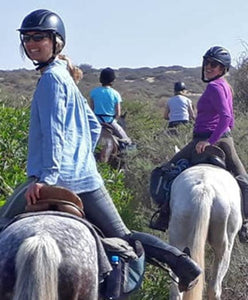 Multiple riders on horseback from behind. The two closest riders are turned around looking at the camera.